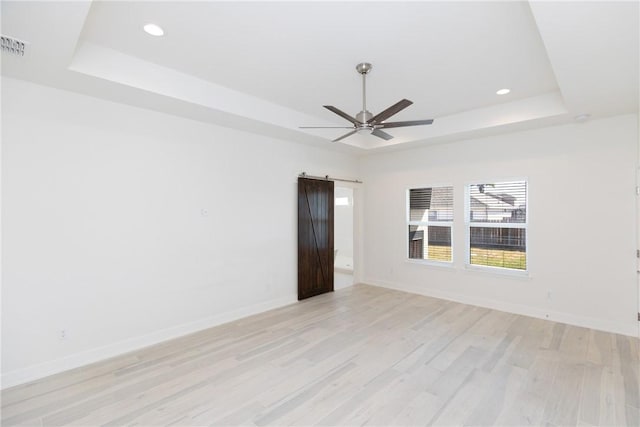 empty room with a barn door, light wood finished floors, baseboards, and a tray ceiling