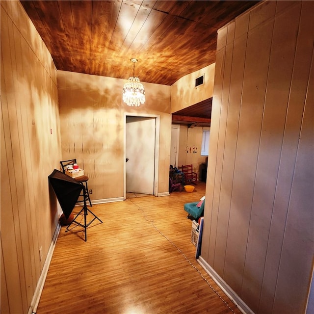 corridor with light wood-type flooring, wood walls, and wooden ceiling