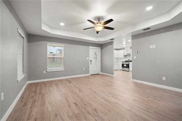 unfurnished living room featuring a tray ceiling, light hardwood / wood-style flooring, and ceiling fan