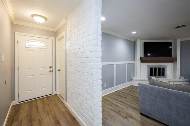 foyer entrance featuring a fireplace, crown molding, visible vents, and wood finished floors