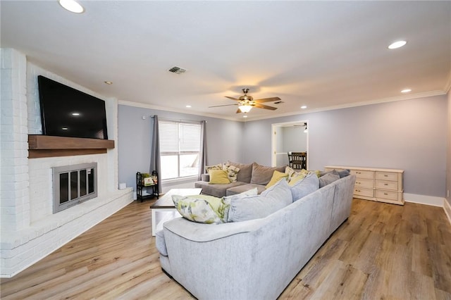 living room featuring visible vents, light wood-style floors, crown molding, a brick fireplace, and recessed lighting