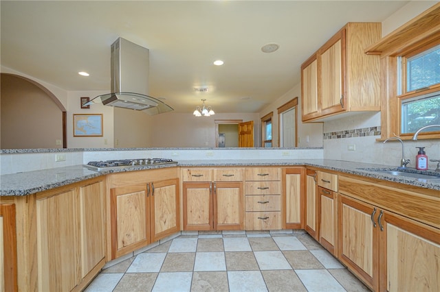 kitchen with stainless steel gas stovetop, island range hood, an inviting chandelier, kitchen peninsula, and sink