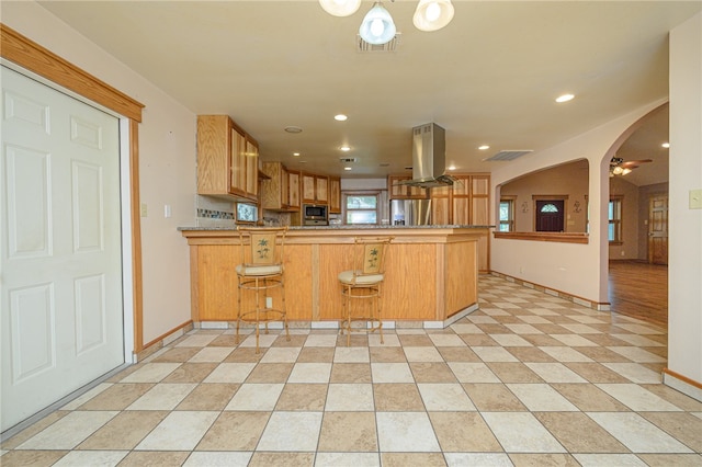 kitchen with appliances with stainless steel finishes, island exhaust hood, a breakfast bar, and kitchen peninsula