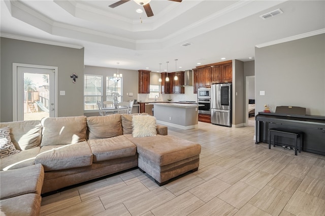 living room featuring ceiling fan with notable chandelier, sink, a raised ceiling, and ornamental molding