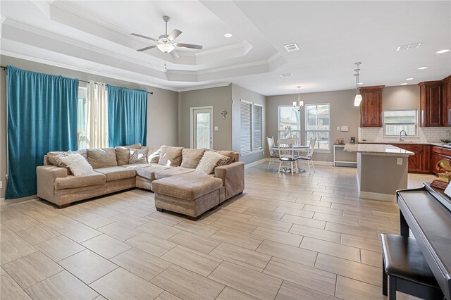 living room featuring ceiling fan with notable chandelier, a raised ceiling, and crown molding