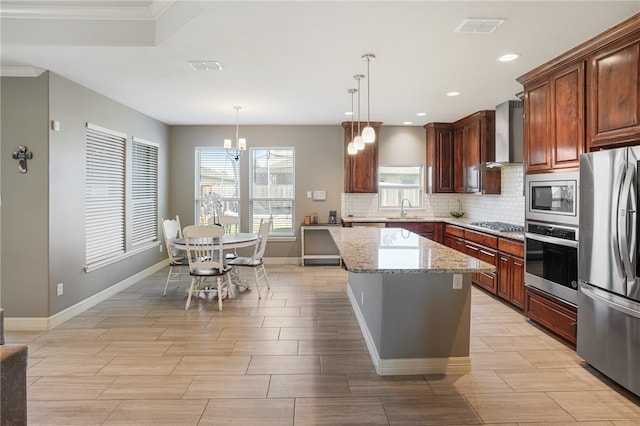 kitchen featuring stainless steel appliances, decorative light fixtures, light stone countertops, wall chimney exhaust hood, and a center island