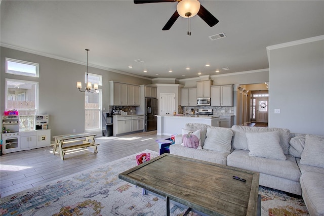 living room with light wood-type flooring, a healthy amount of sunlight, and ceiling fan with notable chandelier