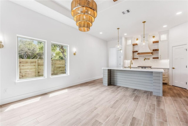 kitchen featuring visible vents, open shelves, light countertops, a sink, and custom exhaust hood