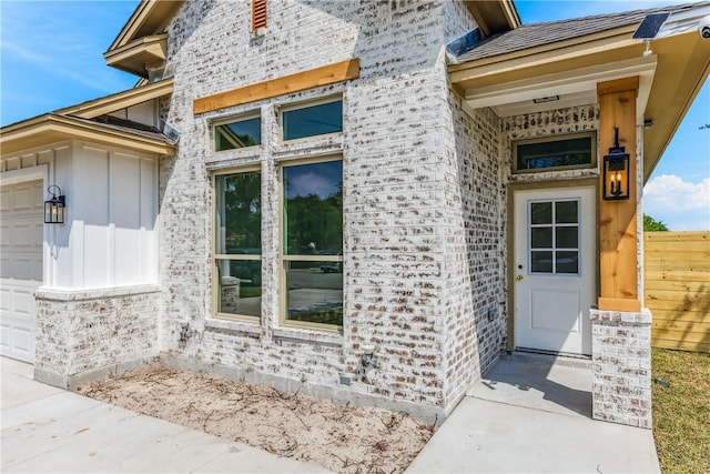 view of exterior entry with brick siding, a garage, and fence
