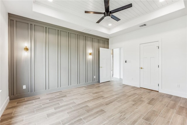 interior space with visible vents, baseboards, a tray ceiling, a ceiling fan, and light wood-style flooring