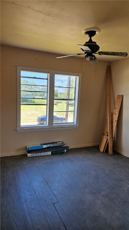 unfurnished room featuring baseboards, dark wood-style flooring, a wealth of natural light, and a ceiling fan