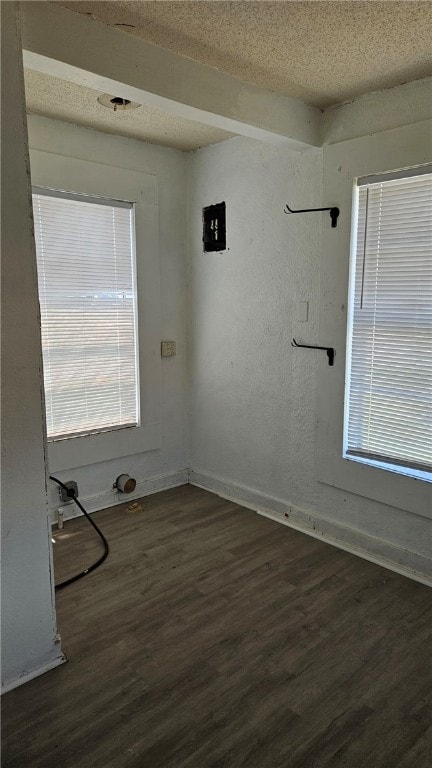 unfurnished room featuring dark wood-type flooring, plenty of natural light, a textured ceiling, and baseboards