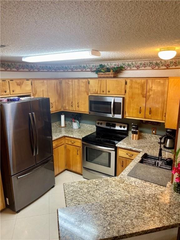 2237 Sunset Cliff Dr, Ingleside, TX 78362 - kitchen with stainless steel appliances, a textured ceiling, light tile patterned floors, a peninsula, and light stone counters