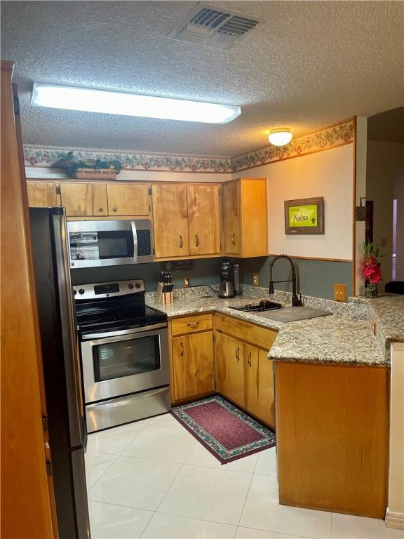 2237 Sunset Cliff Dr, Ingleside, TX 78362 - kitchen featuring appliances with stainless steel finishes, a peninsula, a textured ceiling, a sink, and light tile patterned floors