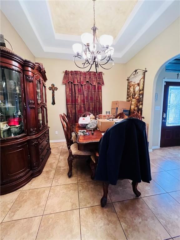 dining room with a raised ceiling, light tile patterned flooring, and an inviting chandelier