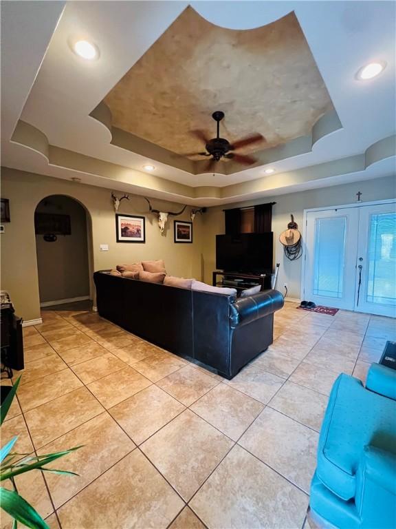 tiled living room featuring ceiling fan, french doors, and a tray ceiling