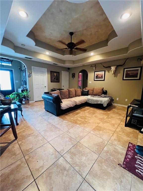 tiled living room with ceiling fan and a raised ceiling