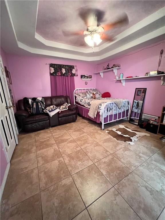 unfurnished bedroom with tile patterned floors, a tray ceiling, baseboard heating, and ceiling fan