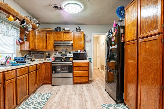 606 N Ironwood Ave, Bishop, TX 78343 - kitchen with stainless steel electric range, freestanding refrigerator, under cabinet range hood, light wood finished floors, and brown cabinets