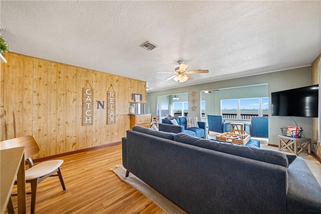 478 S County Road 1144, Riviera, TX 78379 - living room with baseboards, light wood-style floors, wood walls, a ceiling fan, and a textured ceiling