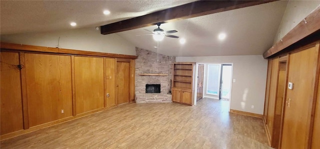 unfurnished living room with a textured ceiling, ceiling fan, lofted ceiling with beams, light hardwood / wood-style flooring, and a stone fireplace