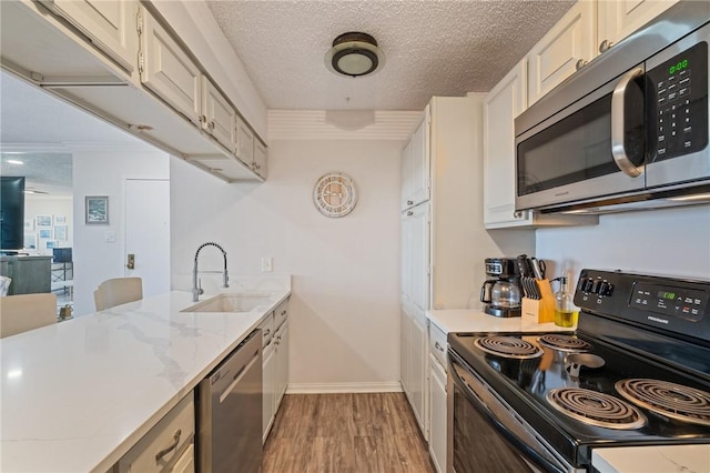 kitchen with wood finished floors, a textured ceiling, a sink, stainless steel appliances, and baseboards