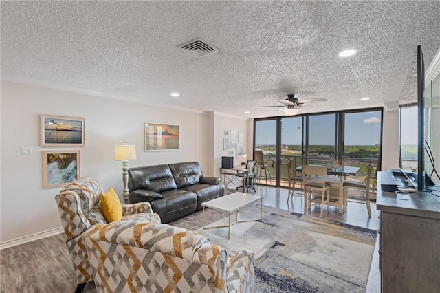 living room featuring wood finished floors, visible vents, a ceiling fan, baseboards, and a textured ceiling
