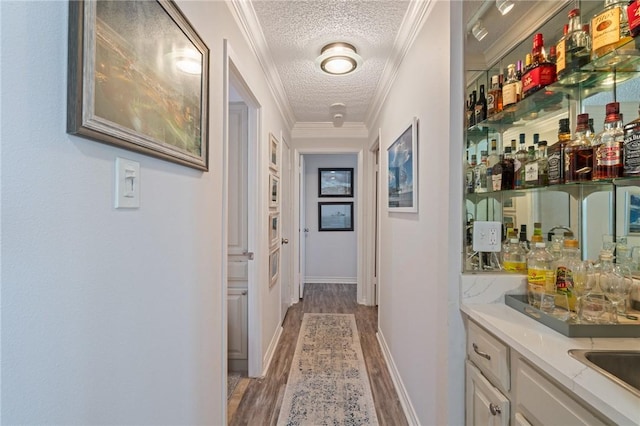 corridor with crown molding, wood finished floors, a textured ceiling, a sink, and baseboards