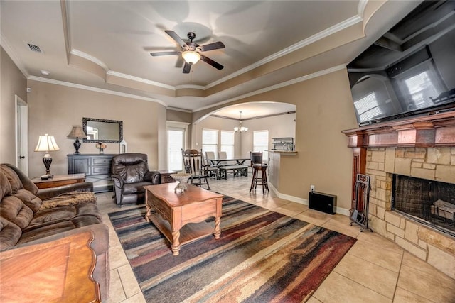 living room with ceiling fan with notable chandelier, a tray ceiling, crown molding, and light tile patterned flooring