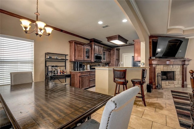 tiled dining space with sink, ornamental molding, a stone fireplace, and an inviting chandelier