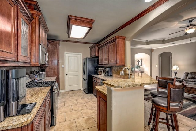 kitchen with stainless steel appliances, tasteful backsplash, light tile patterned flooring, ornamental molding, and a breakfast bar