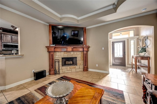 tiled living room with ornamental molding, a raised ceiling, and a stone fireplace