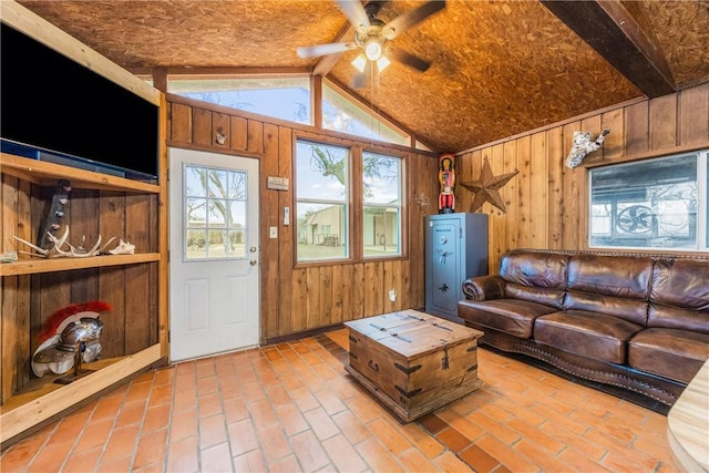 living room with lofted ceiling with beams, brick floor, ceiling fan, and wooden walls