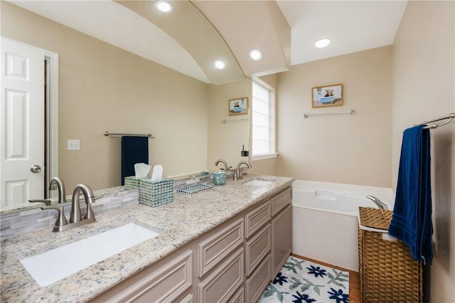 full bath with double vanity, a garden tub, a sink, and recessed lighting