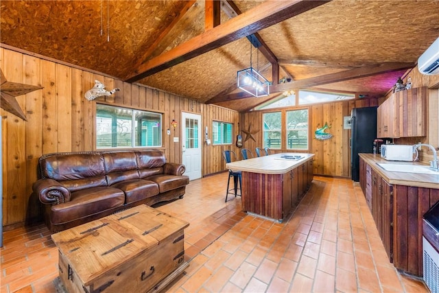 kitchen with vaulted ceiling with beams, wooden walls, a sink, a kitchen island, and open floor plan