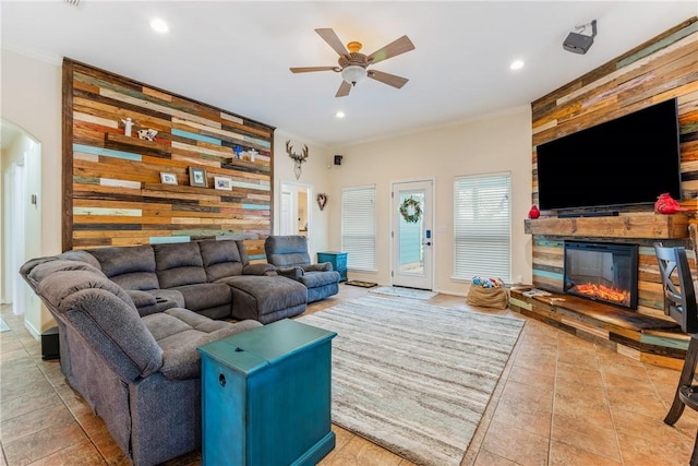 living room featuring arched walkways, an accent wall, wood walls, a fireplace, and ornamental molding