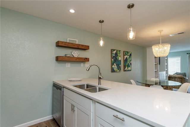 kitchen with a sink, dishwasher, a peninsula, white cabinetry, and a chandelier