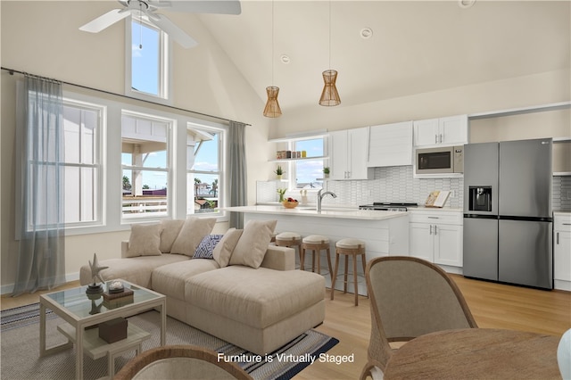 living room with ceiling fan, light hardwood / wood-style flooring, and high vaulted ceiling