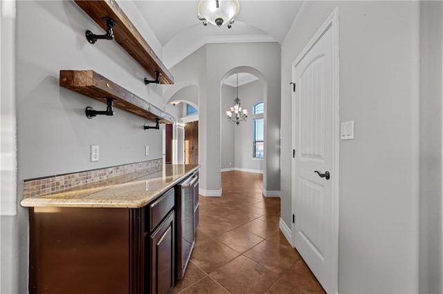 kitchen with dark tile patterned floors, tasteful backsplash, an inviting chandelier, ornamental molding, and dark brown cabinetry