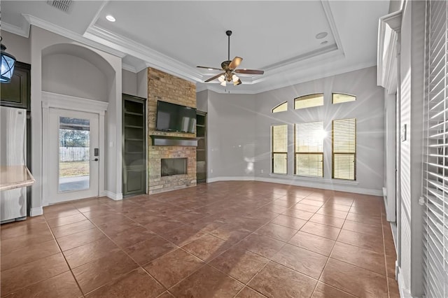 unfurnished living room featuring dark tile patterned flooring, ceiling fan, ornamental molding, a brick fireplace, and a tray ceiling