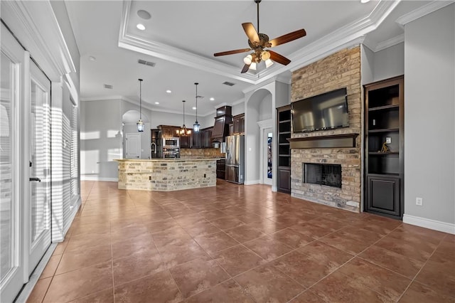 unfurnished living room featuring dark tile patterned flooring, ceiling fan, crown molding, and a stone fireplace