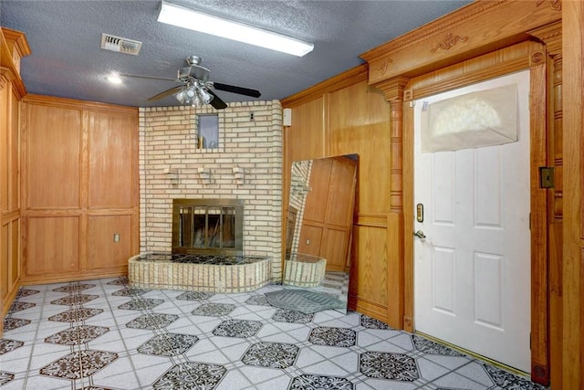 unfurnished living room with wood walls, a textured ceiling, and a brick fireplace