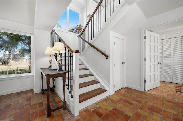 stairs featuring brick floor, a towering ceiling, and baseboards