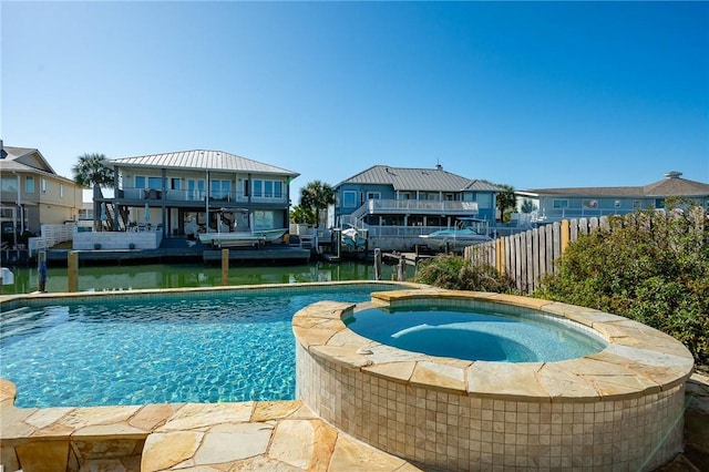 view of swimming pool featuring a water view, a pool with connected hot tub, a residential view, and fence