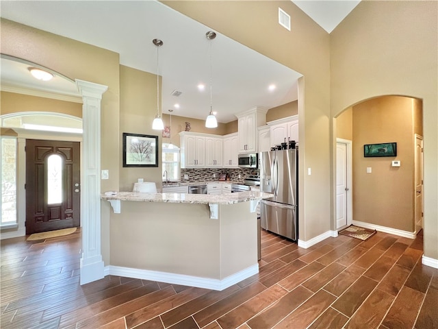 kitchen with light stone countertops, appliances with stainless steel finishes, dark hardwood / wood-style flooring, decorative light fixtures, and white cabinetry