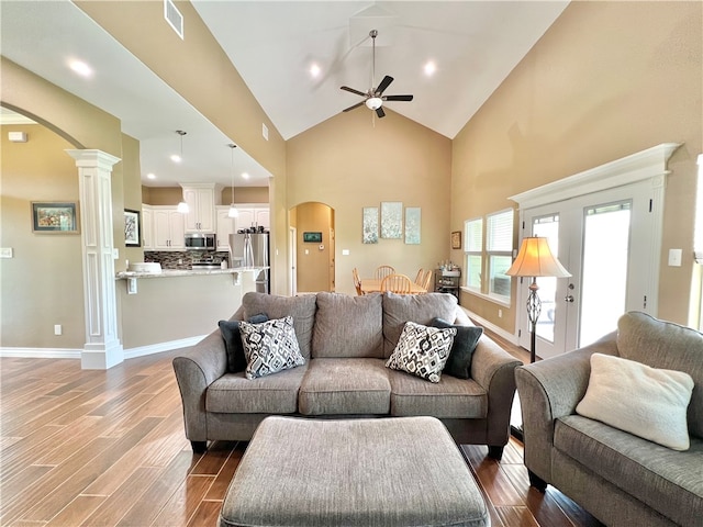 living room with dark hardwood / wood-style floors, ceiling fan, high vaulted ceiling, and decorative columns