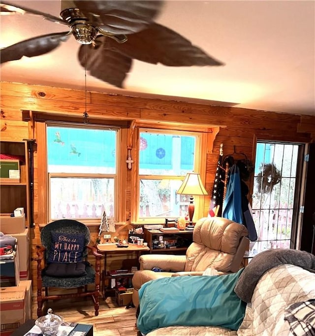 living room with ceiling fan, wood walls, and a healthy amount of sunlight