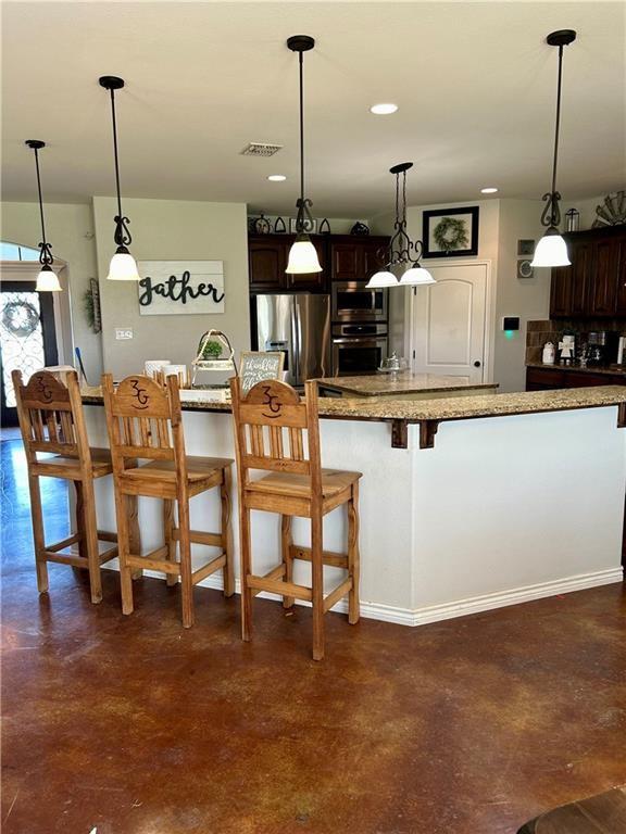 kitchen with dark brown cabinetry, a breakfast bar, visible vents, appliances with stainless steel finishes, and finished concrete floors