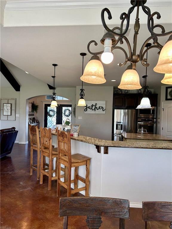 kitchen featuring light stone counters, arched walkways, stainless steel appliances, finished concrete floors, and a kitchen bar