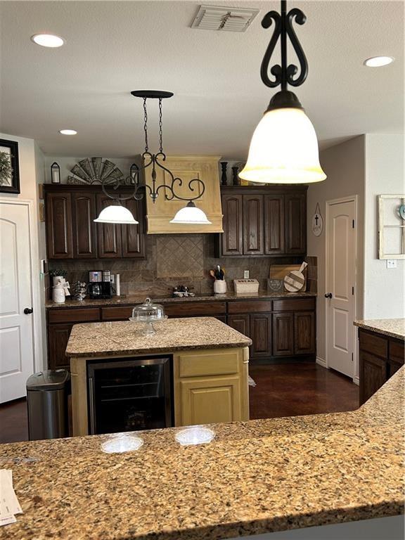 kitchen featuring wine cooler, visible vents, decorative backsplash, light stone countertops, and a center island with sink